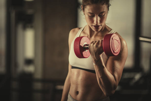 schweißtreibende sportliche frau mit hanteln im fitnessstudio trainieren. - bizeps fotos stock-fotos und bilder