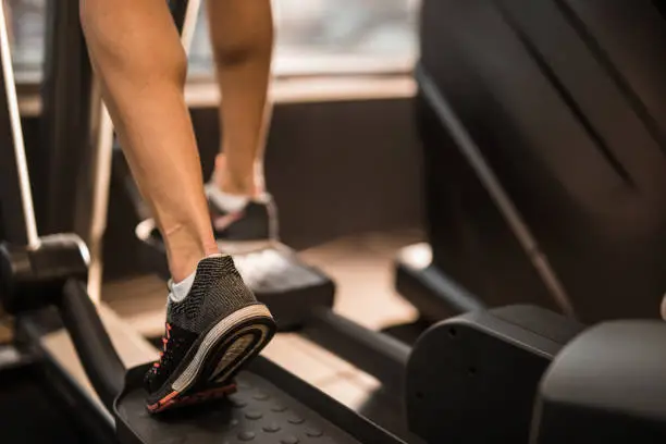 Close up of unrecognizable sportswoman exercising on cross trainer in a health club.
