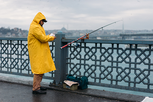 Istanbul, Turkey - January 20, 2018: Crowd of local fishermen fishing on Galata Bridge at rain winter day in Istanbul, Turkey