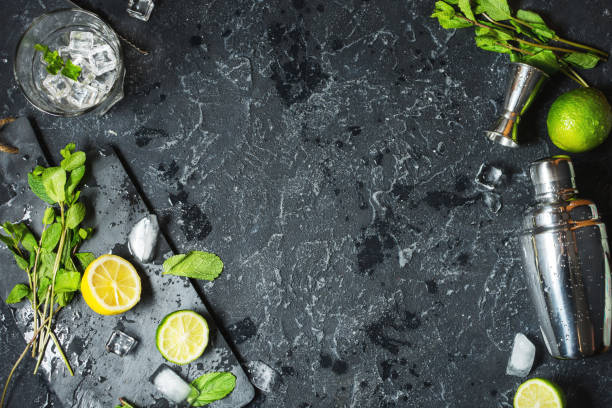 istock Mojito cocktail making. Mint, lime, glass, ice, ingredients and shaker on black stone background 910347794