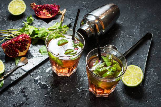 istock Refreshing mojito cocktail with garnet, mint and lime, on a dark gray stone table with shaker for whipping drinks 910348472