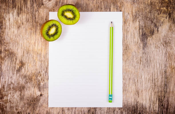 An empty sheet of white paper and pencil. Two halves of juicy kiwi on wooden board. stock photo