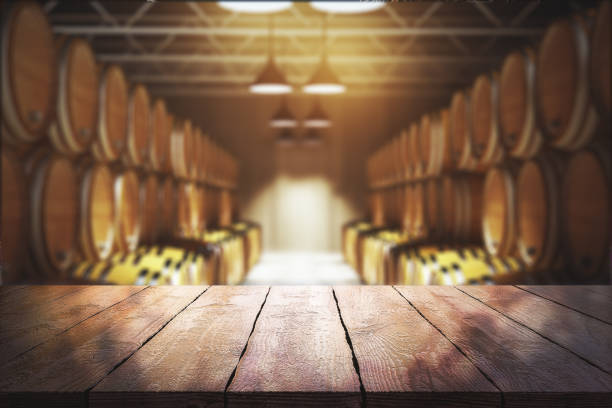 Winery and beverage concept Close up of empty wooden table with blurry wine barrels in the background. Winery and beverage concept. 3D Rendering winery stock pictures, royalty-free photos & images