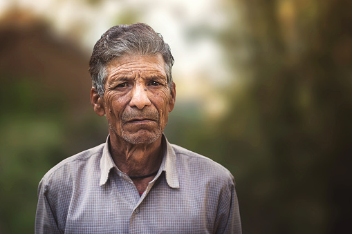 Elderly Indian sixty plus year old man outdoors in nature, looking directly at camera. selective focus, shallow depth of field.