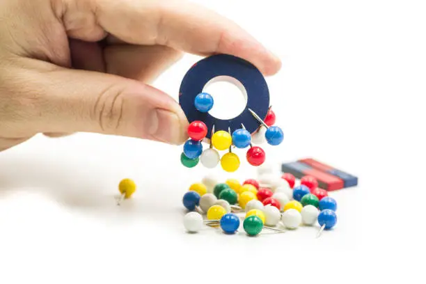 Photo of man hand holding a magnet attracting metal pins