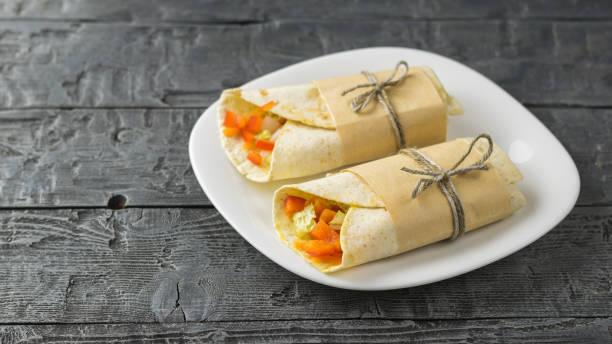 istock Two vegetable roll tortilla from wheat flour in white bowl on a dark wooden table. 910425890