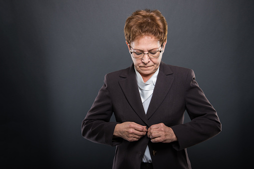 Business senior lady posing buttoning her jacket on black background with copypsace advertising area