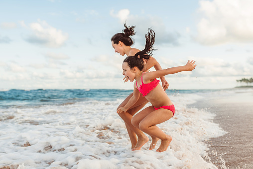 two happy sibling sisters jumping over waves at beach of bahia, brazil