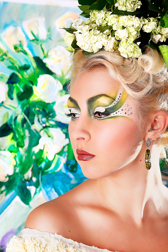 Portrait of a blond pretty girl with bright green white mua, flower bouquet composition on her had, ear-ring, profile, side view. Free place on photo can be used for text inscription, congratulations