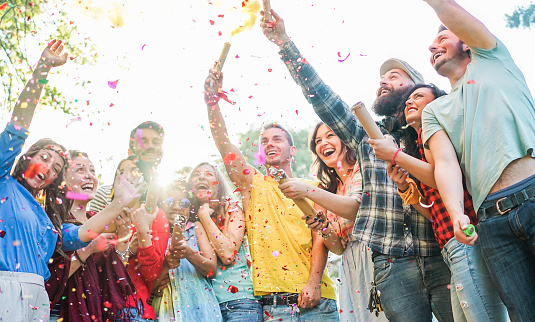 Happy friends having party,throwing confetti and using smoke bombs colors outdoor - Young students laughing and celebrating together - Youth concept - Main focus on three right guys faces