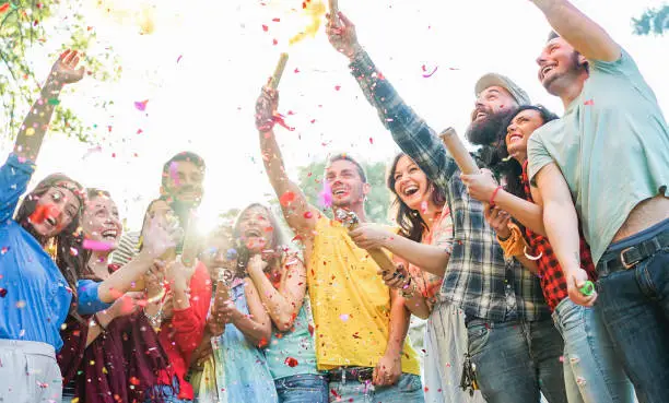 Photo of Happy friends having party,throwing confetti and using smoke bombs colors outdoor - Young students laughing and celebrating together - Youth concept - Main focus on three right guys faces