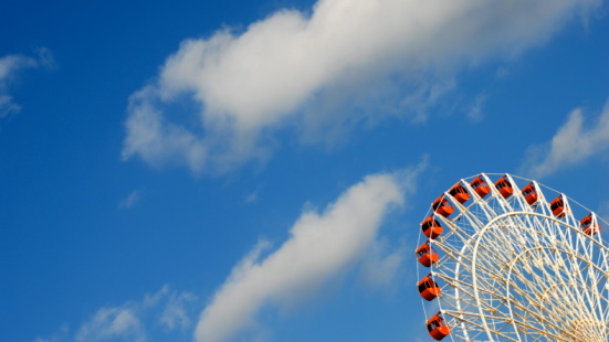 Ferris Wheel with bright red cars against a blue sky background with clouds.