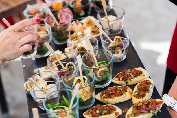 Bruschetta with vegetables, pancakes with salmon Female hand takes snacks: bruschetta made of white bread with seasoned vegetables, rolls of pancakes with red salmon in glass in a row on a tray on a table at a birthday party, anniversary or wedding restaurant food canapes appetizers stock pictures, royalty-free photos & images