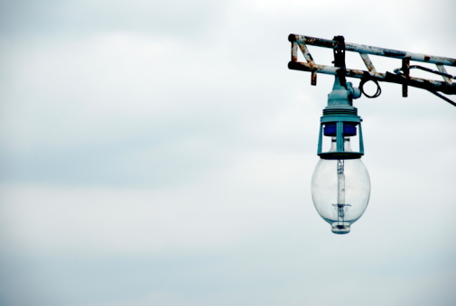 Photo of a large light bulb against a cloudy sky with blue tint added for effect.  