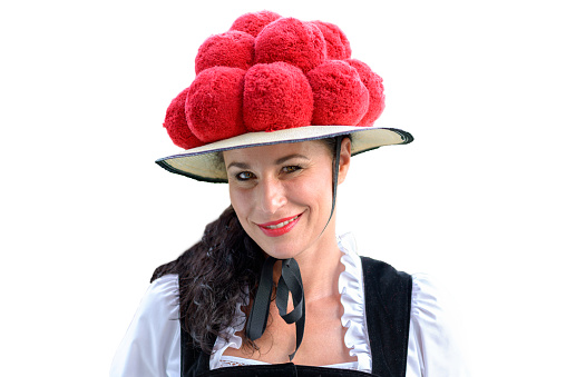 Attractive young woman wearing a traditional Black Forest Bollenhut with its 14 pompoms as she smiles at the camera, before white background