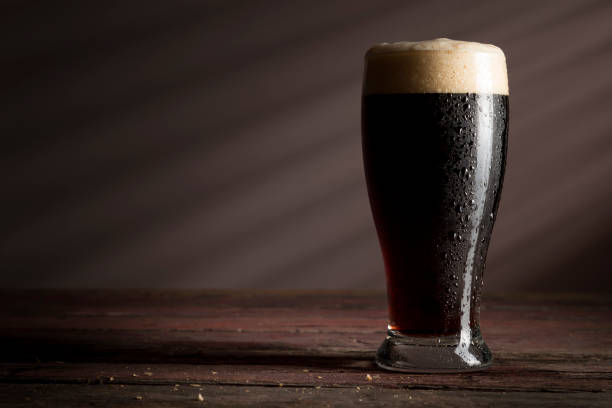 Glass of dark beer Wet glass of cold dark beer with foam placed on a rustic wooden table. porter photos stock pictures, royalty-free photos & images