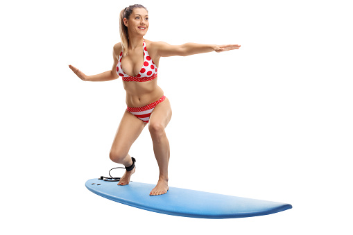Full length portrait of a young woman in bikini surfing isolated on white background