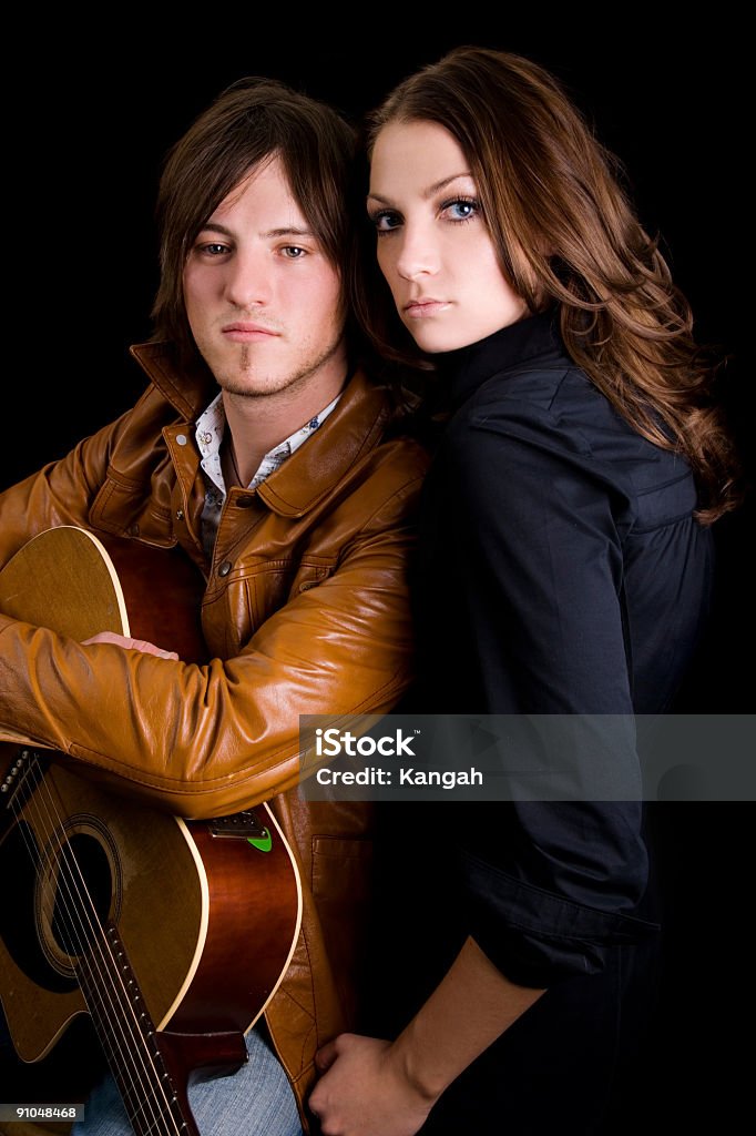 Musical Couple Portrait of a young couple looking into the camera.  Male is holding onto a guitar. Isolated onto a black background. 20-24 Years Stock Photo