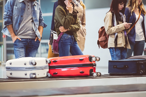 People waiting at baggage claim line terminal of the international airport. Airplane travelers waiting for luggage from a conveyor belt.