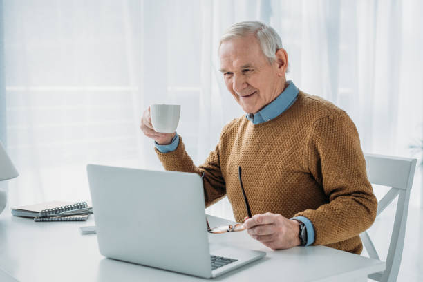 Senior confident man working on laptop and holding coffee cup