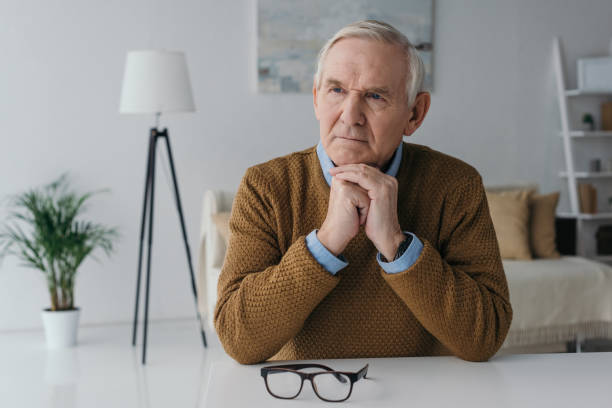 istock Senior thoughtful man sitting by the desk in light room 910493804