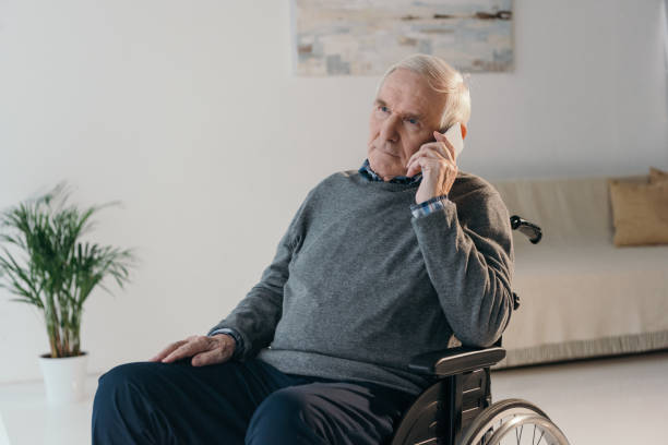 istock Senior man in wheelchair making a phone call in empty room 910499408