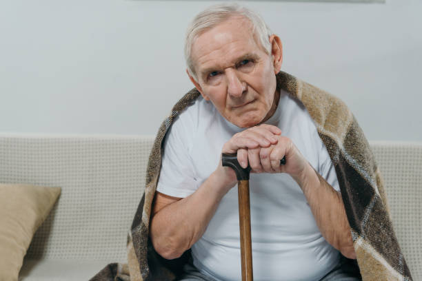 istock Senior man wearing plaid leans on a cane while sitting on sofa 910500080