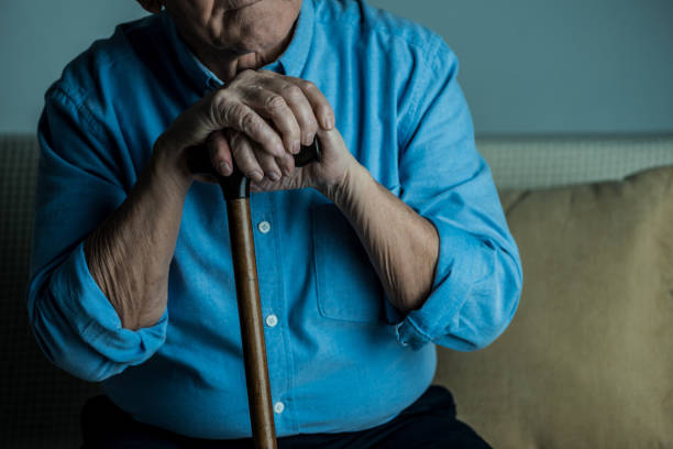 istock Close-up view of senior man leans on a cane while sitting on sofa 910502600