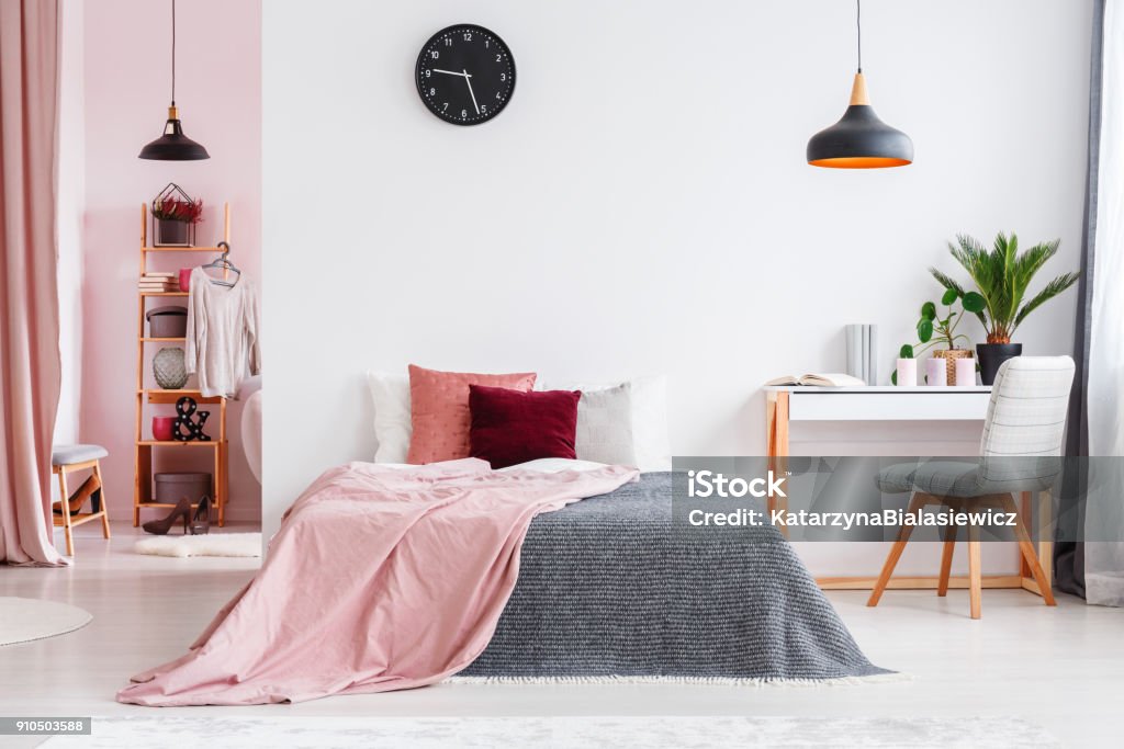 Pink bedroom interior with chair Pink blanket on bed next to desk and grey chair in bedroom interior with black lamp and clock Bedroom Stock Photo