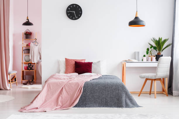 Pink bedroom interior with chair Pink blanket on bed next to desk and grey chair in bedroom interior with black lamp and clock pink bed stock pictures, royalty-free photos & images