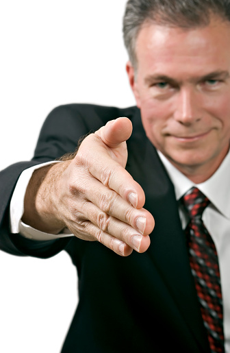 Man in business suite offering his hand in a posture of greeting or agreement.