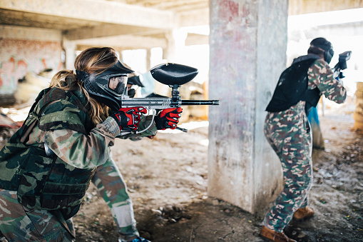 Group of people, playing paintball on a rural terrain in abandoned building.