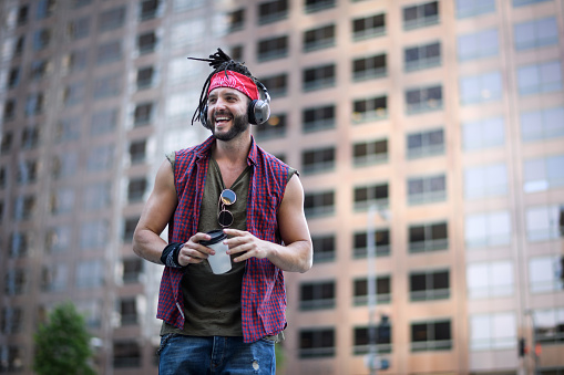 Portrait of young male hipster with headphones and coffee cup having fun in the city.