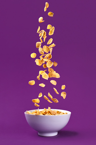 Falling granola in bowl. Healthy breakfast ingredients. Flying food on purple background. Still life. Copy space