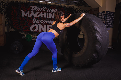 Powerful, attractive muscular girl engaged in gym, training with giant tires in the gym. The athlete pushes a large wheel.