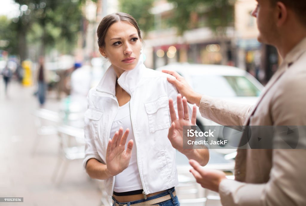 Unhappy girl getting rid of unwelcome stranger outdoors Portrait  of unhappy girl getting rid of unwelcome stranger outdoors Harassment Stock Photo