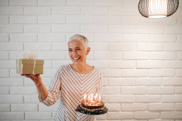 Birthday comes with many surprises Mature woman holding a birthday cake and a gift woman birthday cake stock pictures, royalty-free photos & images