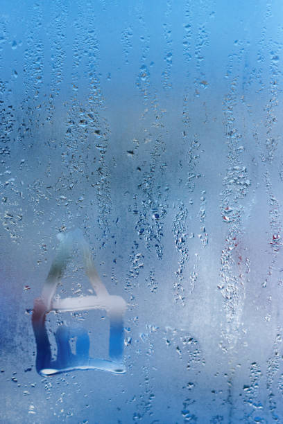 istock Hand draw on glass and water drop. Condensation and raindrops on a window, shallow depth of field. 910560708