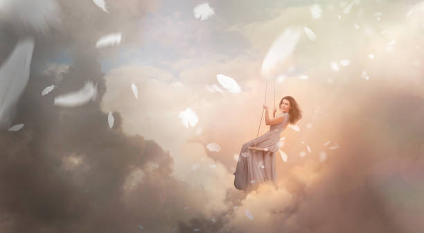 istock Woman swinging in sky with falling feathers 910575038