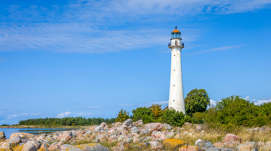 Kihnu island lighthouse in Estonia. Stand alone single white lighthouse stones green forest summer blue sky