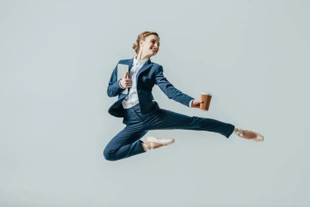 Photo of businesswoman in suit and ballet shoes jumping with coffee and digital tablet