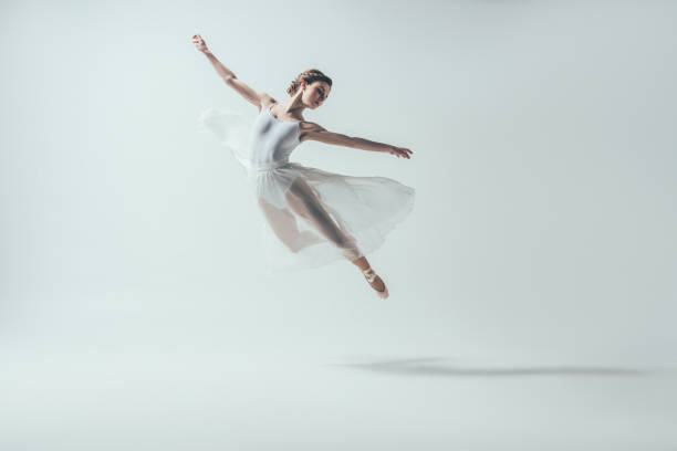 elegant ballet dancer in white dress jumping in studio