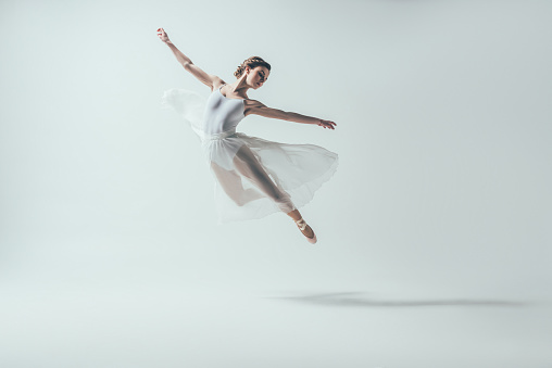 elegant ballet dancer in white dress jumping in studio, isolated on white