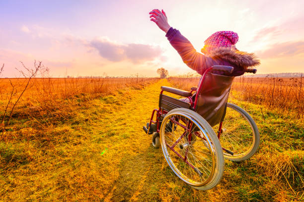 glückliche frau bei sonnenuntergang. ein junges mädchen im rollstuhl - rückansicht - disabled accessible boarding sign stock-fotos und bilder