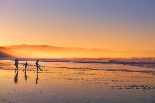 kids silhouette playing and having fun in beach at sunset stock photo