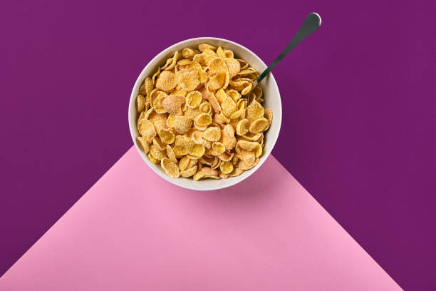 istock Bowl with corn flakes and spoon on purple and pink background, top view 910619850