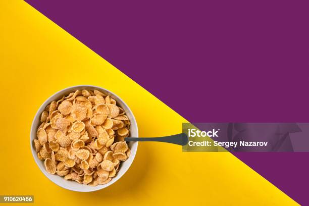 Bowl With Corn Flakes And Spoon On Purple And Yellow Background Top View Stock Photo - Download Image Now