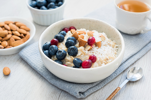 Oatmeal porridge bowl with blueberries, cranberries and almonds and cup of green tea. Concept of healthy lifestyle, healthy eating, fitness menu and dieting