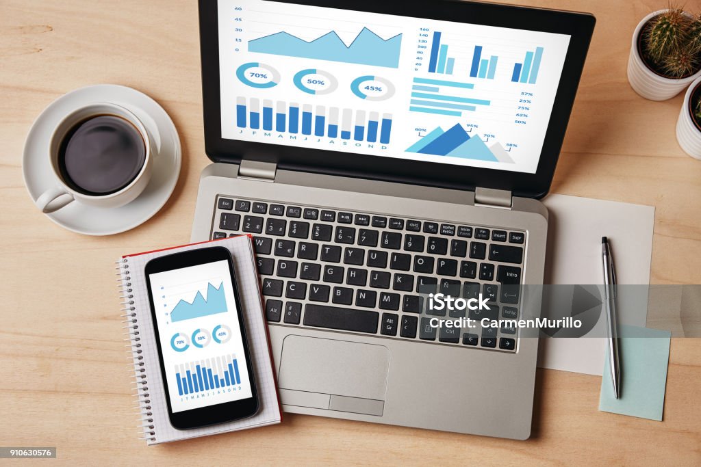 Graphs and charts elements on laptop and smartphone screen Graphs and charts elements on laptop and smartphone screen over wooden table. All screen content is designed by me. Flat lay Work Tool Stock Photo