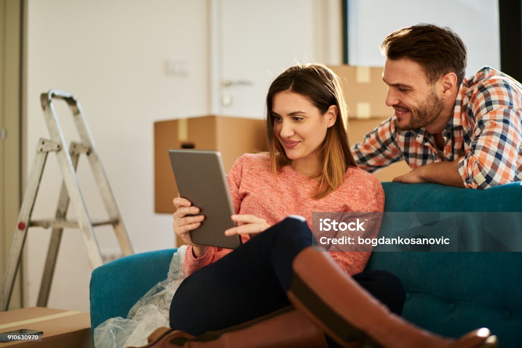 Couple in new apartment Young heterosexual couple surrounded with unpacked cardboard boxes resting on the sofa in their new apartment and looking at digital tablet. Digital Tablet Stock Photo